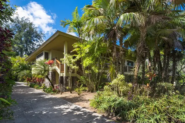 Wooden home exterior sits among tropical trees, paths, and greenery