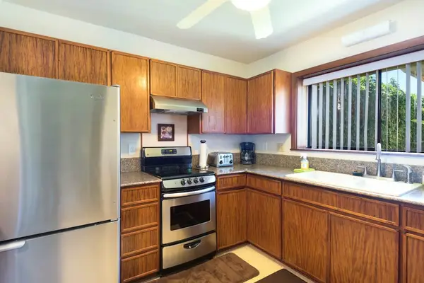 Modern kitchen features stainless appliances, wood cabinets, and bright windows