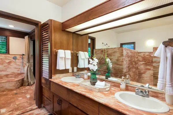 Stone bathroom features a vanity, mirror, open shelving, and glass shower