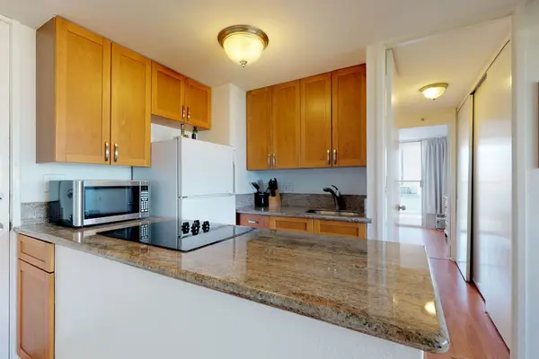 The convenient cooking area includes a flat-top electric stove and a microwave, seamlessly connecting to a hallway that leads through the unit.