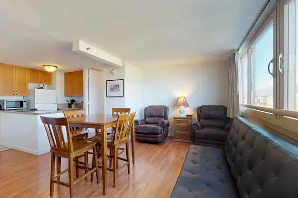 The main living space features wood-style flooring, a dark tufted sofa, two leather recliners, and a tall wooden dining table for gathering.