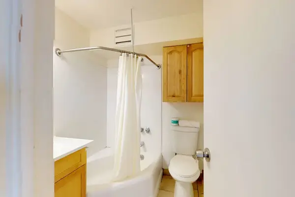 The full bathroom provides a clean and functional space, featuring a standard shower and tub combination, neutral tile flooring, and a convenient wall-mounted wooden cabinet for extra storage.