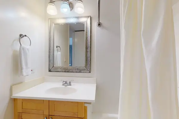 Freshen up at the well-lit bathroom vanity, which highlights a crisp white countertop, a stylish metallic framed mirror, and a warm wooden base cabinet.