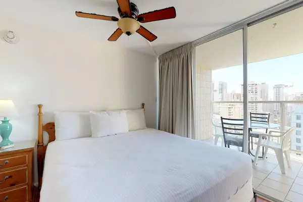 The primary bedroom offers direct sliding-door access to the balcony, a cooling ceiling fan, and lovely elevated city views.