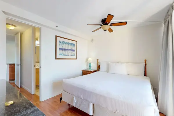 Rest easily in this well-lit bedroom, finished with warm wood-style flooring, tropical framed artwork, and straightforward access to the adjacent bathroom.
