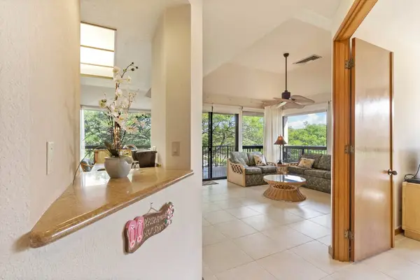 Open-concept living space shows seating, kitchen access, windows, and artwork