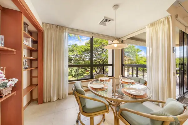 Sunlit dining area features table, chairs, artwork, windows, and kitchen