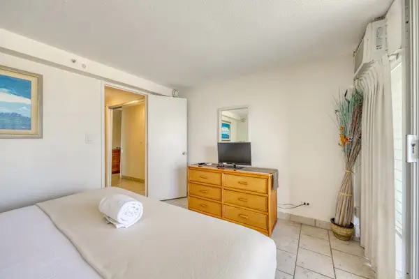 Bright and spacious bedroom with a TV, dresser, and peaceful island-inspired décor for a restful stay.
