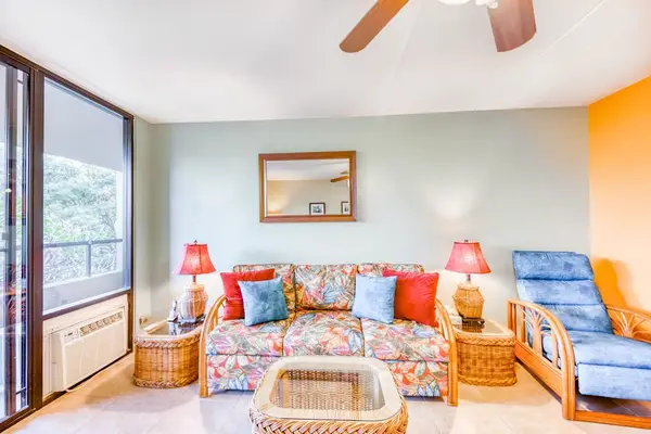 Spacious living area featuring a comfortable sofa, wicker coffee table, blue accent lounger, and massive sliding doors to the balcony! 🛋️🪟