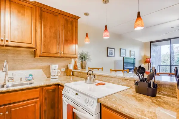 Functional kitchen cooking space featuring a white stove, rich wood cabinets, smooth countertops, and overhead pendant lighting! 🍳💡
