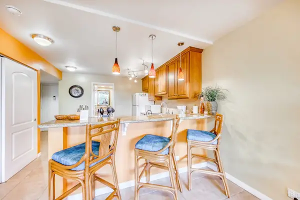 Spacious kitchen island breakfast bar featuring three wooden barstools with bright blue cushions and elegant overhead pendant lighting! 🍳🪑✨🌴