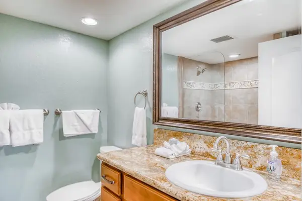Bright bathroom vanity featuring stone countertops, rich wood cabinetry, an oversized wall mirror, and convenient guest towel racks! 🚿💡