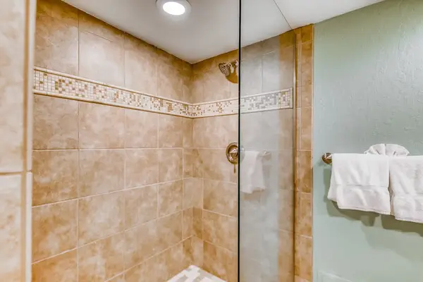 Walk-in bathroom shower featuring warm stone wall tiling, a custom decorative border, glass partition, and recessed ceiling light! 🧼📐