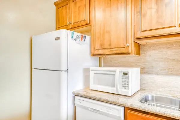 Fully equipped kitchen nook featuring a white refrigerator, microwave, built-in dishwasher, and elegant wood cabinetry storage! 🎛️🏠