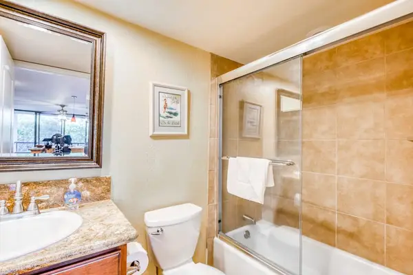 Complete full bathroom featuring a bathtub-shower setup, tiled walls, clean vanity mirror reflection, and wall-mounted artwork! 🛁📐