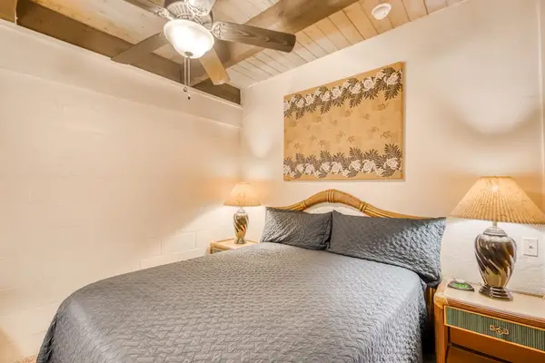 Detailed bedroom perspective showcasing a cozy bed, decorative nightstand lamp, artistic wall hanging, and a cooling overhead ceiling fan! 🛏️🌀✨🌴