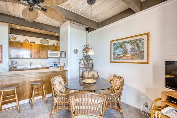 Spacious dining area featuring a woven table set, framed artwork, and an open kitchen breakfast bar with wooden counter stools! 🍽️🪑✨🌴😎