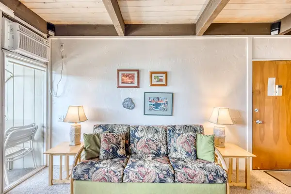 Spacious living room featuring a comfortable patterned couch, dual side lamps, framed artwork, and beautiful rustic wooden ceiling beams! 🛋️🎨✨🌴😎