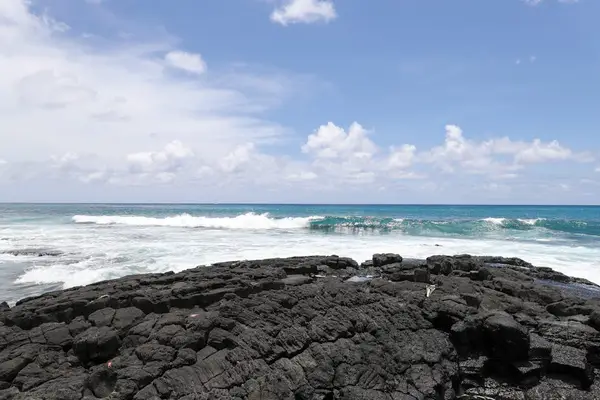 Beautiful tropical coast view featuring rugged volcanic rock, a soft white sand beach, and crashing turquoise ocean waves under a sunny sky! 🌊🏖️☀️