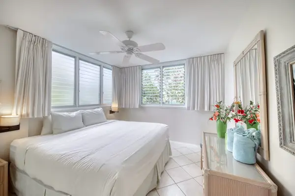 Spacious bedroom presents a comfortable bed, ceiling fan, and curtains