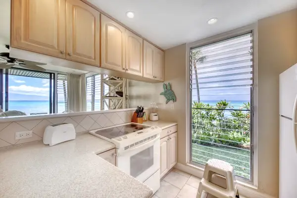 Modern kitchen features wood cabinetry, tiled backsplash, and ocean glimpses