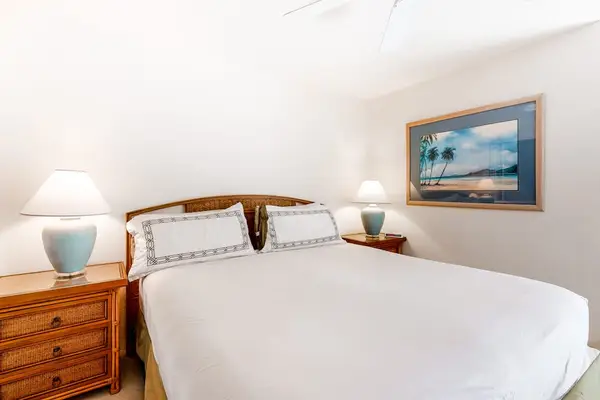 First bedroom features neatly made bed bedside lamps and artwork