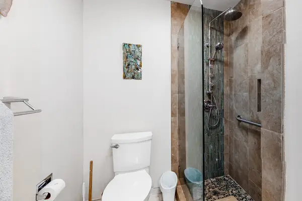 Full bathroom features glass shower toilet and white tile finishes
