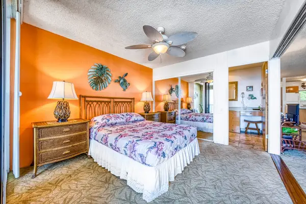 Cozy bedroom featuring a comfortable bed, bedside nightstand, ceiling fan, and mirrored closets