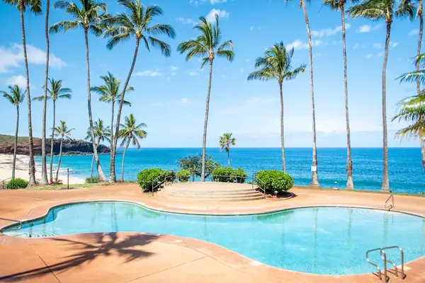 Sunlit resort pool overlooks the Pacific Ocean amid tropical surroundings