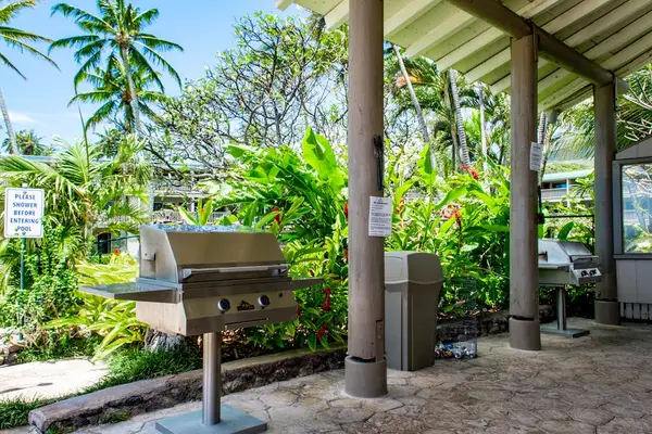 Outdoor grill stands beneath covered lanai surrounded by tropical greenery