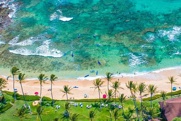 Aerial view of the turquoise waters gently wash onto the white sandy beach at Kiahuna Plantation Resort, creating the perfect backdrop for a relaxing day by the ocean.