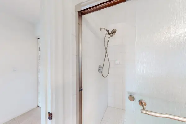 Shower features handheld fixture, grab bar, and clean tiled walls