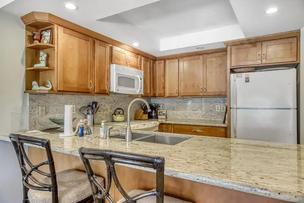 Bright galley kitchen features cabinetry polished counters and practical appliances