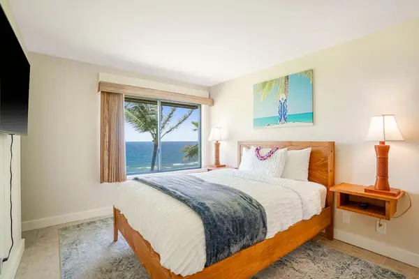 Cozy bedroom featuring a queen bed, warm lighting, and tropical ocean views