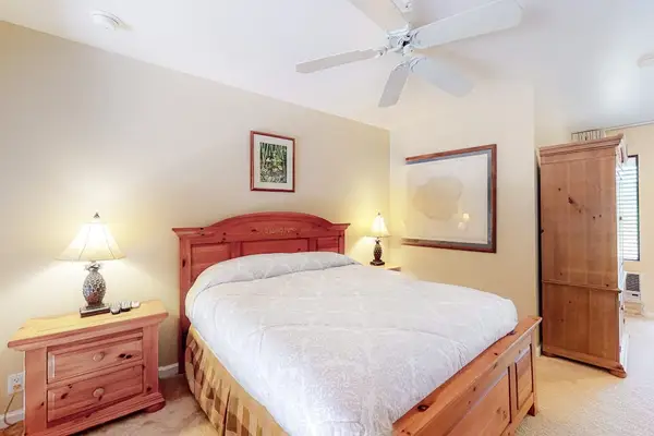 First bedroom features queen bed ceiling fan dresser and lighting
