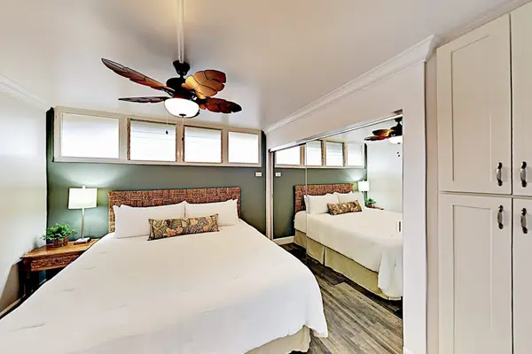 Spacious bedroom offers comfortable bedding, ceiling fan, and calming artwork