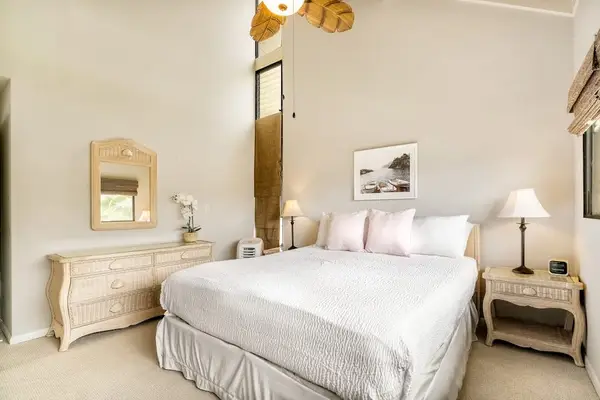 An alternate angle of the primary bedroom showing a large dresser with a mirror and convenient bedside storage