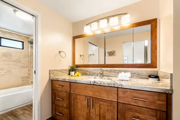 The spacious primary bathroom featuring a wide wooden vanity, large framed mirror, and bright lighting