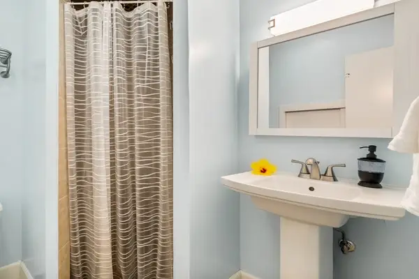 A bright guest full bathroom featuring a classic pedestal sink and a large vanity mirror