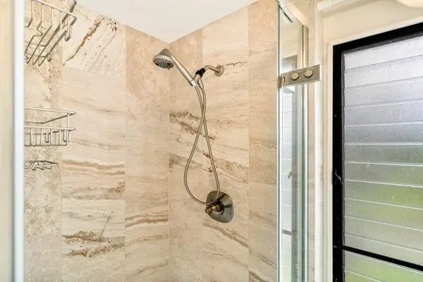 A modern walk-in shower featuring elegant tiling and a flexible handheld showerhead attachment