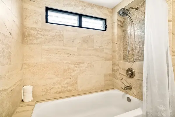 A full bathtub and shower combination in the primary bathroom, accented by elegant stone tiling