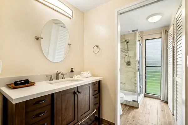 A bright and modern bathroom featuring a spacious vanity, round mirror, and a glass-enclosed walk-in shower