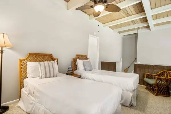 A welcoming twin bedroom layout featuring comfortable beds with woven headboards and a warm standing lamp