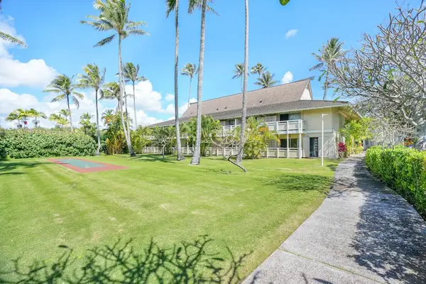 Paved pathway leading past manicured lawn and palm trees