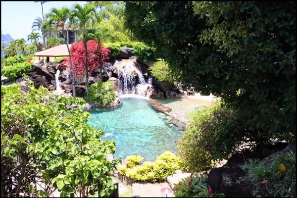 Waterfall flows through lush greenery, rocks, and peaceful landscaping