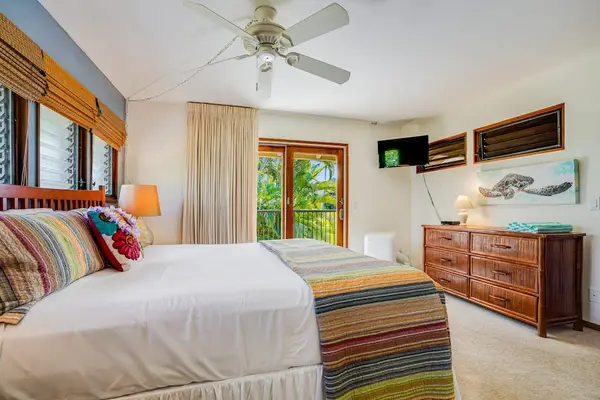 Spacious Bedroom Setup featuring Wooden Dresser, Mounted TV & Ceiling Fan