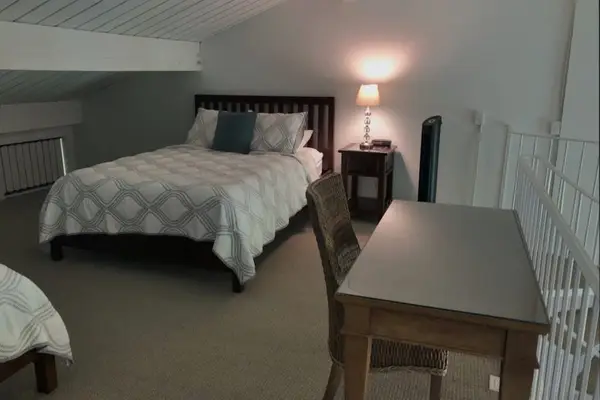 Loft bedroom includes comfortable bedding, desk, chairs, and soft carpeting