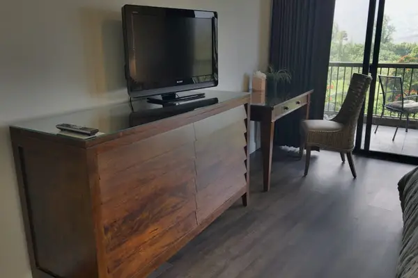 Spacious bedroom sitting area includes television, desk, chair, and balcony doors