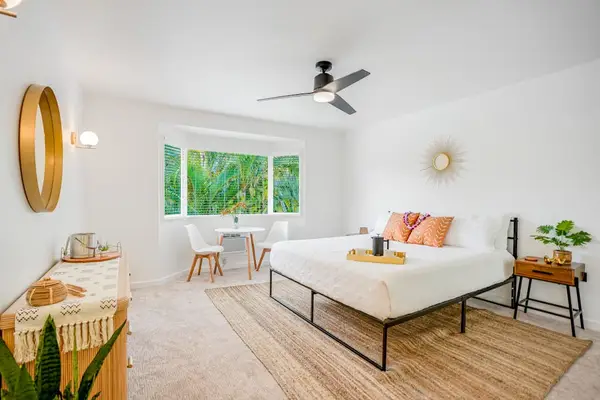 Spacious primary bedroom featuring a king bed, ceiling fan, and large windows with tropical views