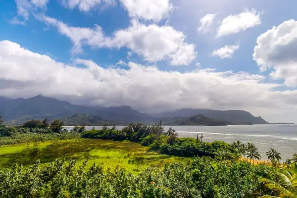 Mountain landscape overlooks lush fields, sparkling waters, and dramatic clouds